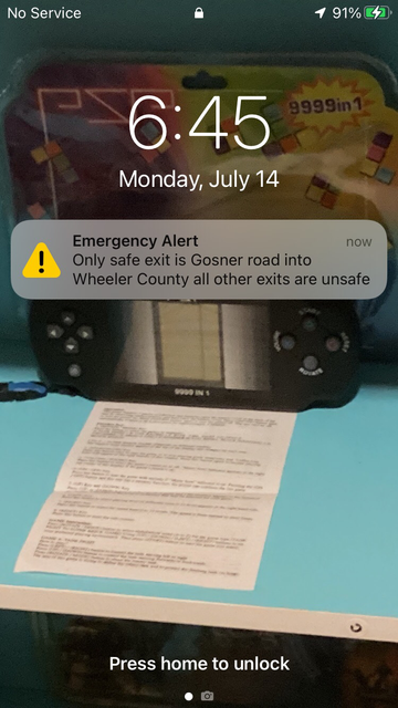 Emergency alert on an iPhone Lock Screen reading “Only safe exit is Gosner road into Wheeler County all other exits are unsafe”. The phone has no service.