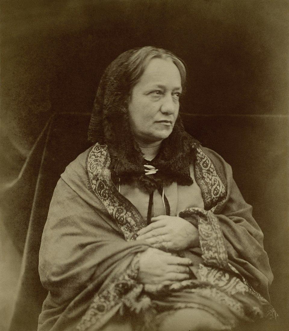 Title: Julia Margaret Cameron Artist: Henry Herschel Hay Cameron (British, 1852–1911) Date: 1870 Medium: Albumen silver print from glass negative  This is a photographic portrait of Julia Margaret Cameron, the renowned Victorian photographer, who was also the mother of the photographer, Henry Herschel Hay Cameron.  Julia is shown in a three-quarter view, facing slightly to her left (viewer’s right). Her head is gently turned, eyes looking off-camera with an introspective, almost mystical expression, characteristic of how she posed her own subjects.  https://en.wikipedia.org/wiki/File:Julia_Margaret_Cameron_MET_DP114480_-_Restoration.jpg