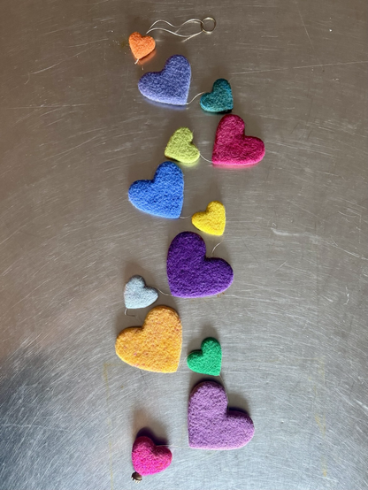 A string of multi coloured and sized needle felted hearts on a stainless steel table top