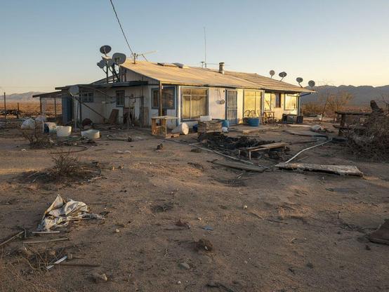 Abandoned house with nine satellite dishes in sunrise light.