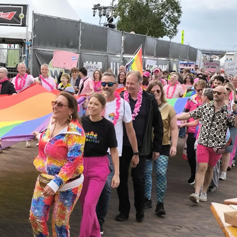 Optocht met allemaal kleurige mensen, waar ik ook tussensta met roze broek en zwart shirt van de Budapest Pride. We dragen meterslange Pride Vlag mee. 