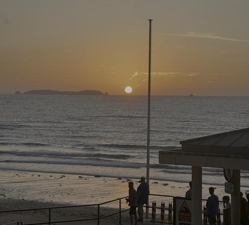 Die Sonne steht am goldroten Himmel tief ganz rechts. Das Meer rollt langsam wieder an, die Flut ist am steigen. Ein Fischer steht am spiegelnden Sandstrand und hat seine Rute ausgeworfen.