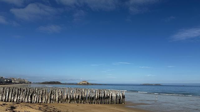 Das Meer bei Ebbe weit draussen, der Strand unterbrochen von den wellenbrechenden, eingerammten, uralten und verdrehten Eichenstämmen, sieht man weit hinten einen Teil der Altstadt, das vorgelagerte Fort und das alles unter stahlblauem Himmel.