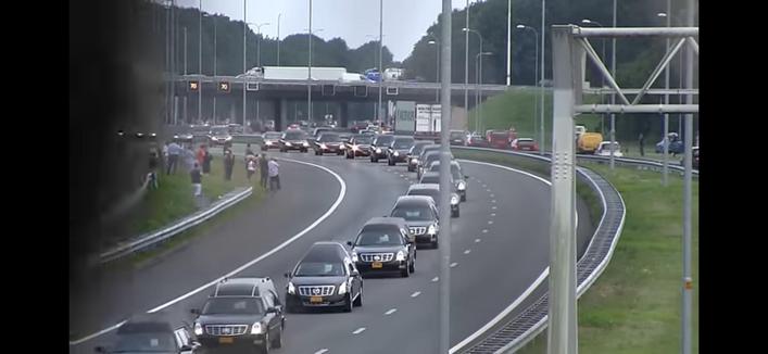 Een eindeloze rij zwarte rouwwagens op een snelweg. Personen staan in de berm.