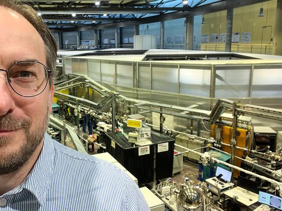 Selfie (Gesicht halb links angeschnitten) vor sehr technisch anmutenden Röhren und Gerätschaften im Hintergrund.