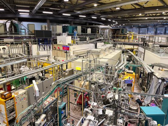 Großer hallenartiger Raum, der mit technischem Gerät, Apparaturen aller Art und Röhren gefüllt ist.