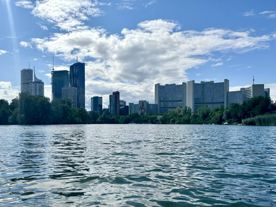 View across the water to the starting point, directly at the UNO City, the United Nations Office in Vienna/Austria. Skyscrapers, blue sky, some larger clouds.
