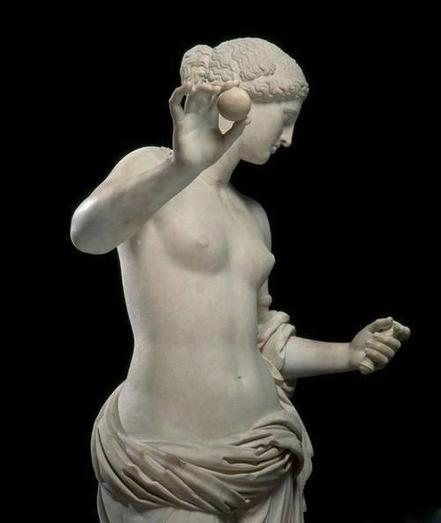 Roman marble sculpture of Venus. The goddess holds an apple in her right hand, raised to about chin-height, and the remains of a handle in her left, possibly the handle of a mirror. Her hair is styled in a beautiful braided bun. She is topless, but cloth is draped around her hips.