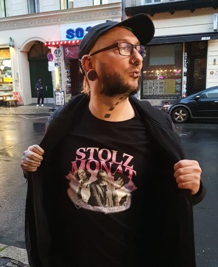 Schwarzes Shirt mit pinkem Aufdruck "Stolzmonat". Dazu sind abgebildet drei Held*innen queerer Geschichte.