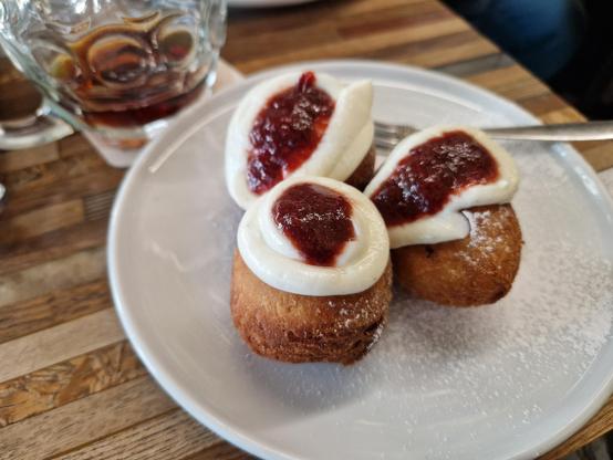 Three spherical doughnuts on a plate, topped with a circle of white and a blob of red. 