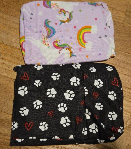 A square with unicorns and rainbows above a larger rectangle with paw prints and hearts on a wooden floor.