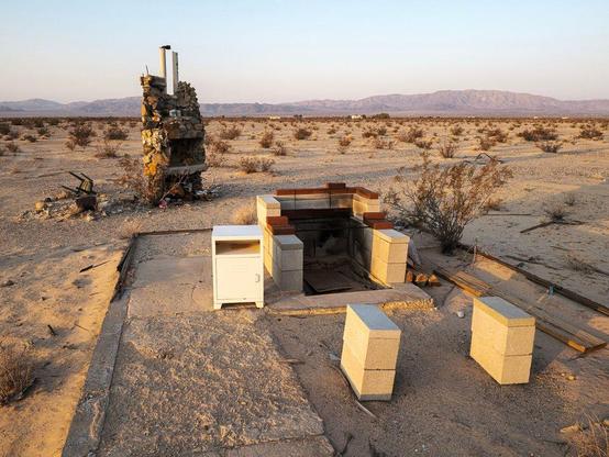 Fireplace with cooking grill and second fireplace with chimney in desert landscape.