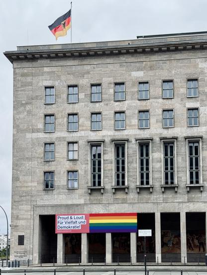 Gebäude des Bundesfinanzministeriums mit deutscher Flagge und Pride-Banner “Proud & Loud: Für Vielfalt und Demokratie!” an der Fassade