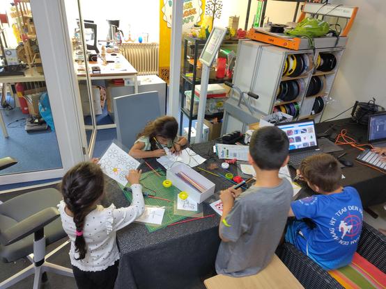 Kids using 3d pens to make stuff. Girl holding a sheet with flowers.