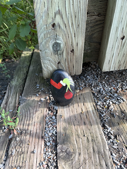 A painted rock depicting the grinches arm and hand stealing a Christmas tree ornament. 