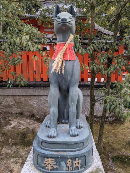 A kitsune statue has an offering of heads of rice wrapped around its neck. Foxes are familiars of the 'rice god' Inari.
