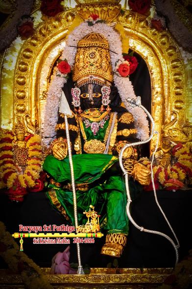 Idol of Hindu deity Krishna in green seated with left leg down and right leg folded at the knee and placed over the left knee. Krishna wears gold shoes, gold palm coverings, gold crown, and lots of gold ornaments; holds a silver bow in left hand and a silver arrow in right hand. A gold arch behind Krishna. A string of white flowers around Krishna from his left waist to the right waist, going over the crown.