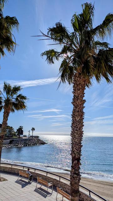 Blick auf die Promenade, Palmenstrand und Reflexion der Sonne auf dem blauen Meer