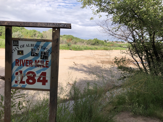 Sign says “City of Albuquerque River Mile 184” against the backdrop of a dry sandy riverbed 