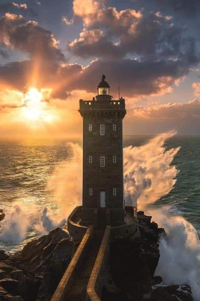 Photo by Le Conquet 
A dramatic picture of waves breaking at the rocks at the front of the lighthouse and a blaze of a setting sun to the left. Photo by Le Conquet 
A dramatic picture of waves breaking at the rocks at the front of the lighthouse and a blaze of a setting sun to the left.
