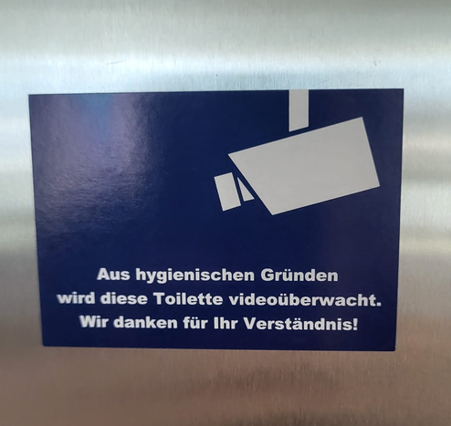 Kleber mit Kamera-Piktogramm, blauer Grund - weisse Schrift. 
Layout sehr ähnlich wie offizielle Piktogramme.
Text:
Aus hygienischen Gründen wird diese Toilette videoüberwacht.
Wir danken für Ihr Verständnis.