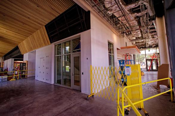 Interior of a building with barricades erected to keep visitors out of areas where construction is still ongoing,  on side there is a wood slat ceiling,  on the other side you can still see a lot of HVAC stuff above.
