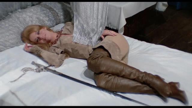 an image of a blonde woman with her hair tied up, laying on a bed next to a silver sword
