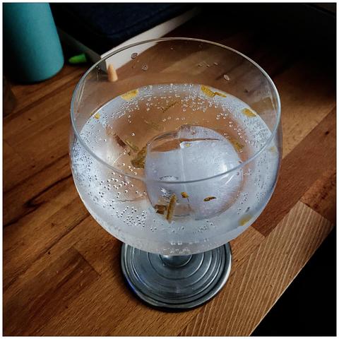 Gin balloon with a large ball of ice and yuzu peel on a wooden desk.