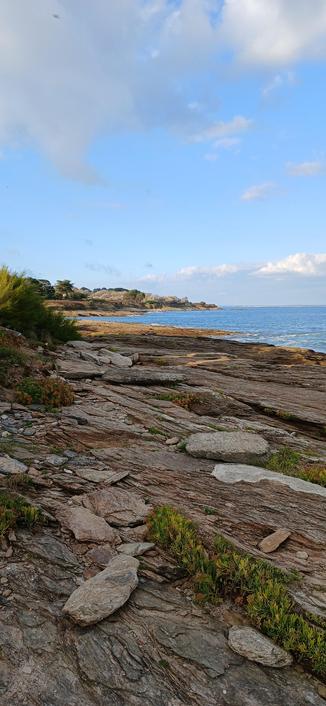 Côte plane et rocheuse de l'Île de Groix, océan au fond, ciel bleu et nuageux