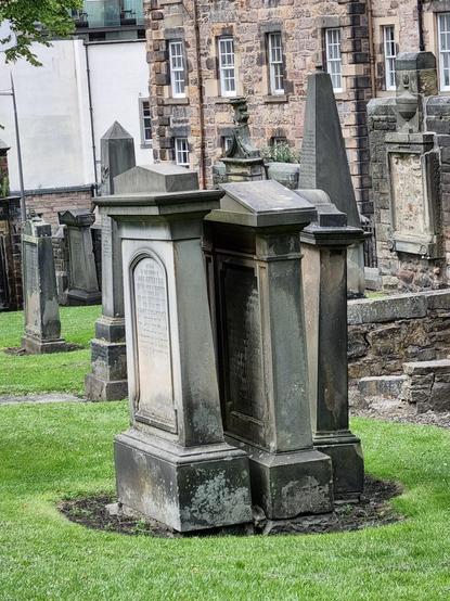 Drei Grabsteine auf einem Friedhof, so dicht voreinander, dass man die hinteren kaum noch lesen kann