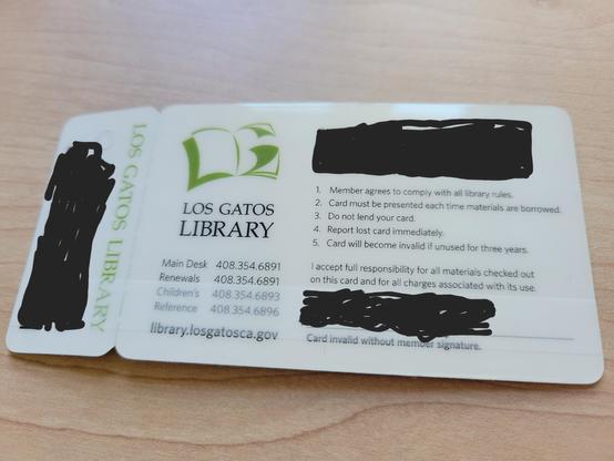 Reverse of plastic library card and attached small keychain library card. The design shows an illustration of a red heart with shelves of books inside it. The background is a gradient from blue at top to yellow at bottom. Script text at top: "Hayward Public Library", and at bottom, "Bibliotecc pūblica de Hayward"