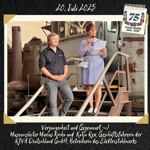 Eine weiblich gelesene Person im gestreiften Kleid steht auf einer Eisentreppe vor einer silberfarbenen Diesellok (DDR-Lok V60) und hält eine Rede. Die Person ist Katja Rex.
Links neben ihr steht eine männlich gelesene Person mit schwarzem Hemd und grauer Hose. Die Person ist Museumsleiter Marius Krohn.