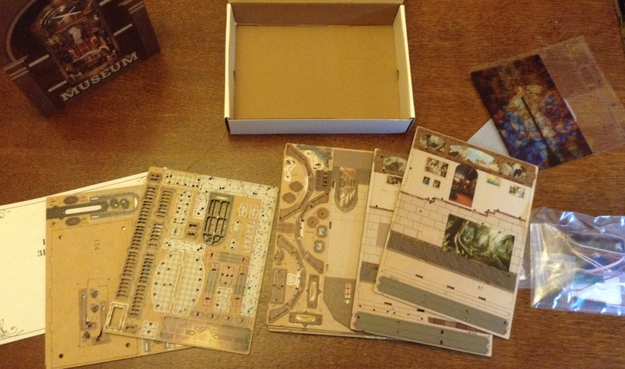 Photo of the contents of a book nook kit showing lots of printed, (presumably) laser-cut, panes of wood, spread out on a table. At the back is part of the box with the word "Museum" on it.
