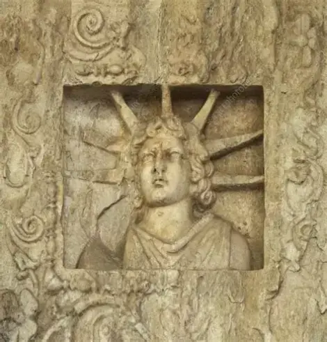 Ceiling coffer from the 'Captives Facade' of the North Basilica of Ancient Corinth. A coffer is a sunken panel in a ceiling that is part of a series of grids that create a geometric pattern. It shows Helios, the Sun, with his iconic seven-spiked sun-ray crown. His hair is curly and of shoulder-length. He wears a chiton or a cloak that would be pinned over his right shoulder but the shoulder chipped off.