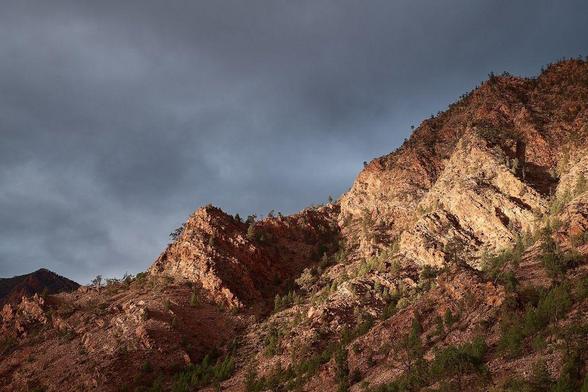 Dramatic light and shadows play on the rugged cliffs of Flinders Ranges during an evening storm, capturing the raw beauty and intensity of the landscape.