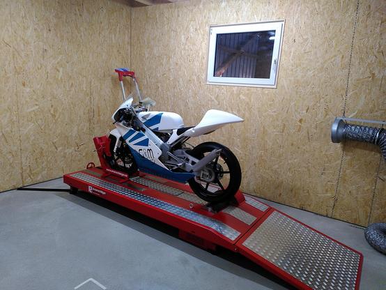 Motorcycle on a Dynamometer. The dyno is red and silver while the bike is white with a blue wing design.