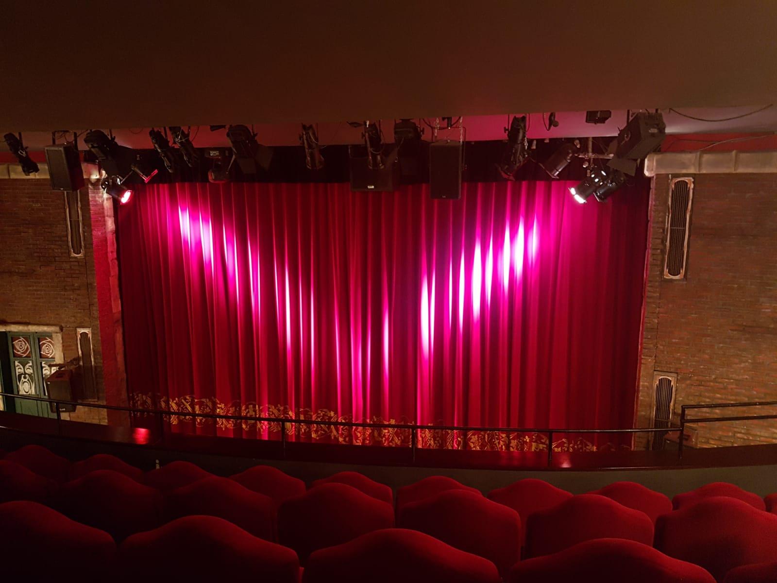 Geschlossener Theatervorhang. Im Vordergrund sieht man leere rote Sitzreihen. Geschlossener Theatervorhang. Im Vordergrund sieht man leere rote Sitzreihen.