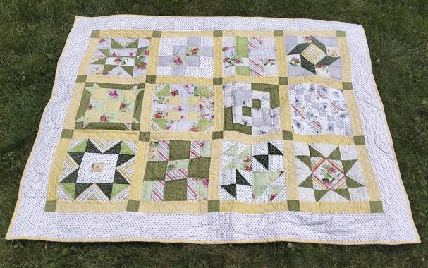 a quilt, it is different shapes divided by yellow bars with green squares at the intersections, the quilt is done with greens and yellows ad some reds and greys on white, a polka dot border 