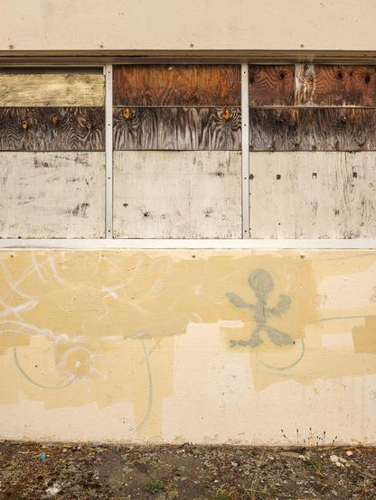 Dilapidated wall with boarded-up windows, layers of roller paint, and a blobby human-shaped graffito.