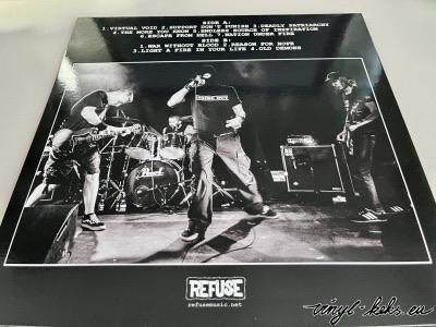 Ein Schwarz-Weiß-Bild einer Live-Band mit vier Musikern, die auf der Bühne auftreten. Der Hintergrund zeigt den Bandnamen "REFUSE" und enthält eine Trackliste mit Songtiteln. Die Szene fängt die Energie eines Live-Musikauftritts ein.