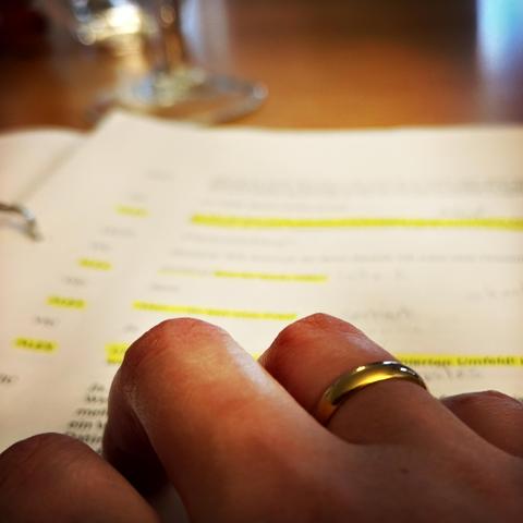 Detailansicht einer rechten Hand mit goldenem Ehering, die auf einem Theaterskript mit gelben Unterstreichungen und Notizen liegt.