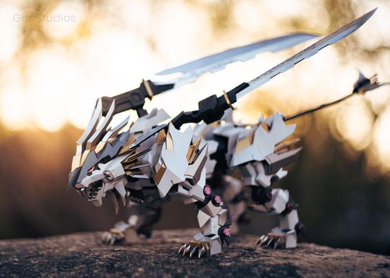 A Mugen Liger Zoid stands posed on a rock, its white and gold armor gleaming in the warm sunset light. Twin swords are mounted on its back, adding to its sleek, futuristic design. The robotic lion’s aggressive stance and sharp detailing give it a powerful, dynamic presence.