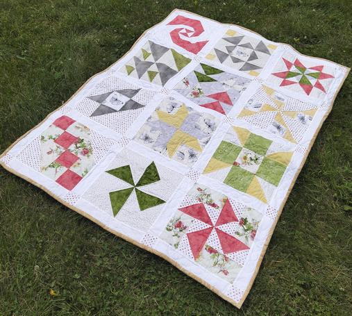 43 x 57 in (109 x 145 cm) a quilt, it is different unique shaped of light red, green, light yellow, and grey against a light background with a thin gold frame around it