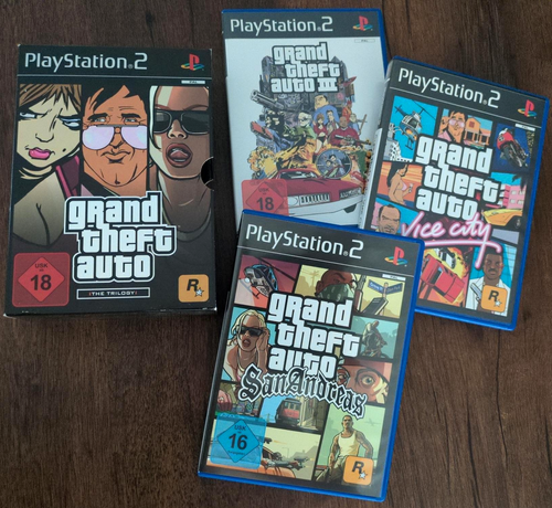 Grand Theft Auto - The Trilogy for PS2 unboxed on a wooden table. There is the trilogy's slipcase and the three individual game cases for GTA III, Vice City and San Andreas