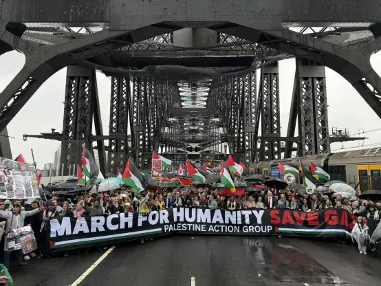 Protesters with Palestinian flags carry a large banner which reads MARCH FOR HUMANITY SAVE GAZA PALESTINE ACTION GROUP  at the Sydney Harbour Bridge.