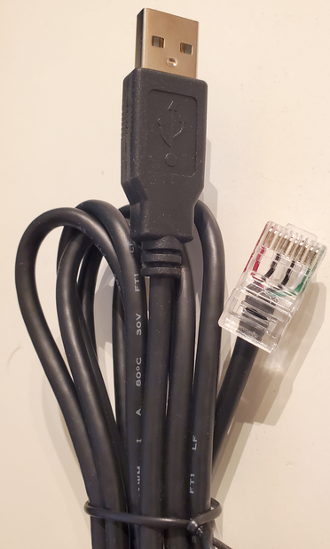 Photograph of a black computer cable, still in its original twist-tie, with a USB-A connector on one end and an RJ-45 (typically Ethernet) connector on the other.