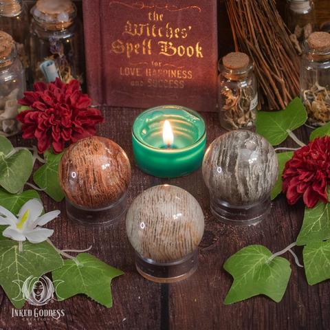 Three specimens of the "Thousand Layer Quartz Sphere" product are arranged on a wooden surface. They are polished spheres made up of many layers of red, brown, white, and green quartz, giving them a tightly striped appearance. Presented by Inked Goddess Creations.