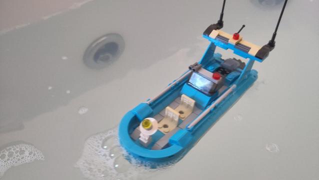 Man sieht ein blaues Polizeiboot aus Klemmbausteinen in einer Badewanne. Von schräg oben aufgenommen. Außerdem sieht man Wasser in der Wanne, etwas Schaum und eine Massagedüse.
