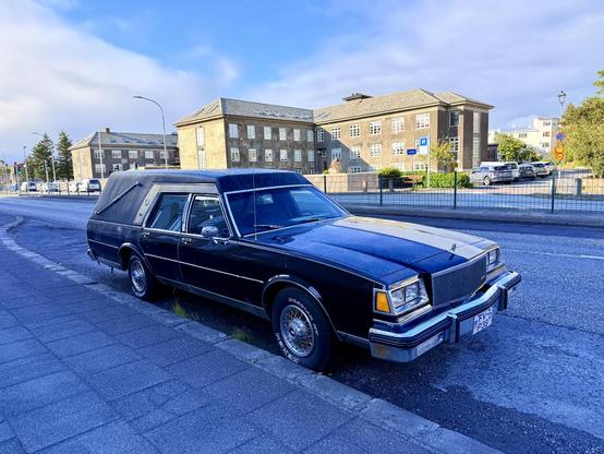 A Buick hearse parked at an apartment building off the main road