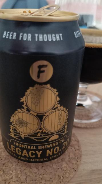 Close-up of Frontaal Legacy 20 BA stout: black can with golden letters. Poured beer in the background.